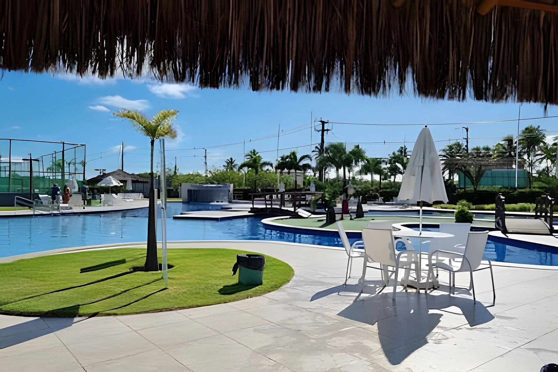 Deck sombreado com mesas, gramado e piscina do Muro Alto Condomínio Clube